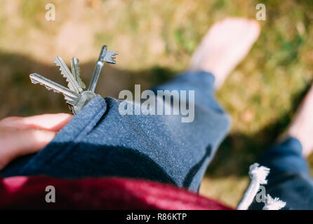 Ansicht von oben in die Tasche in der Hose, aus denen fällt ein Bündel Schlüssel zum Haus. Verlust der Schlüssel aufgrund von Fahrlässigkeit, Sicherheit Probleme. Selektiver Fokus Stockfoto