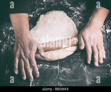 Koch in einem schwarze Tunika, rollt Teig für Pizza, Ansicht von oben Stockfoto