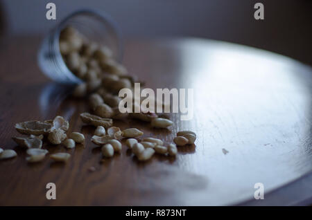 Erdnüsse aus einem Glas alle über den hölzernen Tisch gefallen. Stockfoto