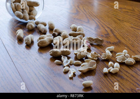 Erdnüsse aus einem Glas alle über den hölzernen Tisch gefallen. Stockfoto