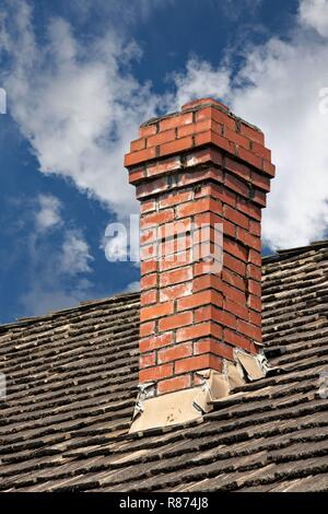 Hohen Schornstein: Rot gemauerten Schornstein sitzt auf einem Strohdach gegen einen bewölkten Himmel. Stockfoto