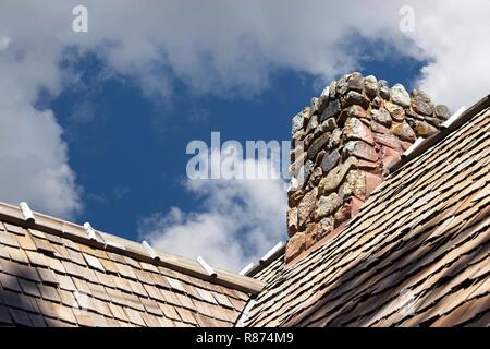 Steinkamin: Einfaches Foto eines stacheligen Steinschornsteins, der aus einem Strohdach gegen einen wolkig-blauen Himmel auftaucht. Stockfoto