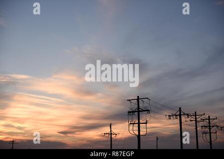 Silhouette des Stromnetzes, Strommasten und elektrische Hochspannungsleitungen, Himmel und Wolken bei Sonnenuntergang in Wyoming, USA Stockfoto