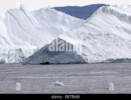 Grönland Disko Bucht: Landschaft mit Eisbergen kleines rotes Ausflugsboot vor mächtigem Eisberg Stockfoto