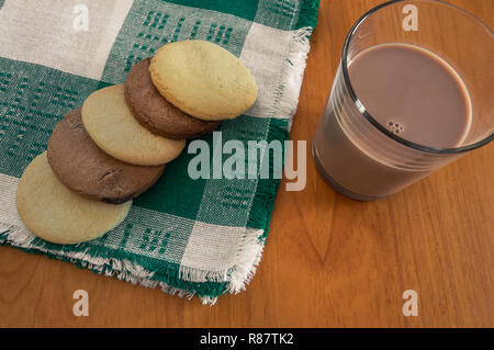 Verschiedene hausgemachte Cookies auf ein Tuch, Serviette und ein großes Glas Schokolade Milchshake auf hölzernen Tisch. Süßes Frühstück oder einen Snack in Home. Ansicht von oben. Stockfoto