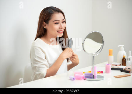 Das Loswerden von Kabelsalat. Schöne junge Frau an ihr Spiegelbild in mirrorand ihr langes Haar bürsten Während am Tisch sitzen Stockfoto