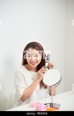 Das Loswerden von Kabelsalat. Schöne junge Frau an ihr Spiegelbild in mirrorand ihr langes Haar bürsten Während am Tisch sitzen Stockfoto