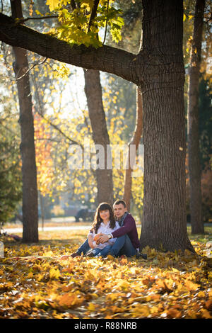 Paar sitzen unter einem großen Baum im Herbst Park Stockfoto