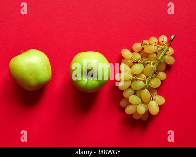 Oben Blick auf isolierte Gruppe von ein grüner Apfel mit einem Bündel Süße kernlose Trauben im Studio mit rotem Hintergrund Stockfoto