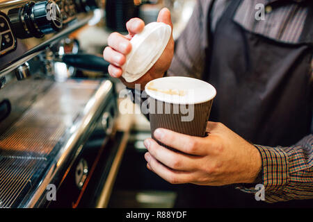 Nahaufnahme von Barista holding Tasse Kaffee und Deckel. Er wird Deckel auf Schale zu setzen. Kerl stand auf der Kaffeemaschine Stockfoto