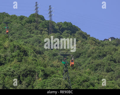 Orange Kabinen einer Seilbahn zwischen zwei Masten, sich gegen das Grün der Berge am Comer See, Italien Stockfoto