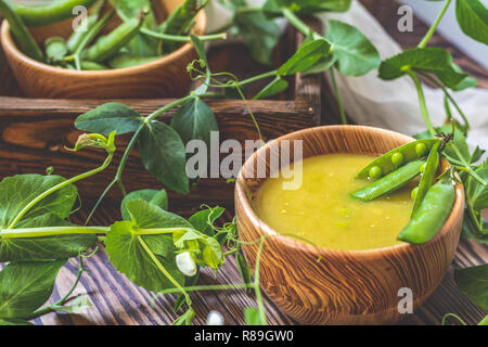 Holz- Teller Erbsensuppe und Hülsen der Frische grüne Erbsen auf einem dunklen Holz- Oberfläche. Vintage Holz- Oberfläche für Design mit wunderschön gelegenen Hülsen der Gre Stockfoto