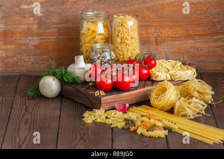 Satz von Zutaten für italienisches Abendessen. Sortiment von Raw-Typen und Formen von Nudeln in Tomaten cherry, Pilzen, Knoblauch, Gewürze Kräuter auf einer hölzernen zurück Stockfoto