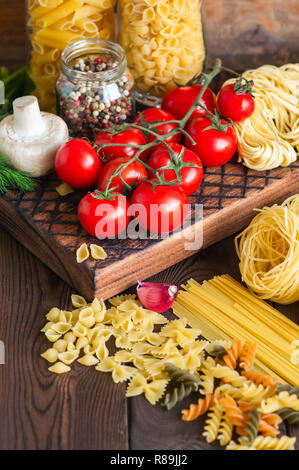 Satz von Zutaten für italienisches Abendessen. Sortiment von Raw-Typen und Formen von Nudeln in Tomaten cherry, Pilzen, Knoblauch, Gewürze Kräuter auf einer hölzernen zurück Stockfoto