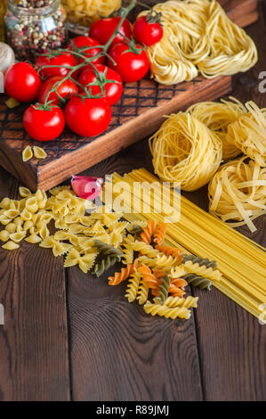 Satz von Zutaten für italienisches Abendessen. Sortiment von Raw-Typen und Formen von Nudeln in Tomaten cherry, Pilzen, Knoblauch, Gewürze Kräuter auf einer hölzernen zurück Stockfoto