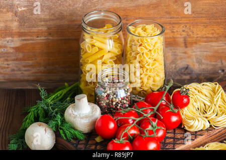 Satz von Zutaten für italienisches Abendessen. Sortiment von Raw-Typen und Formen von Nudeln in Tomaten cherry, Pilzen, Knoblauch, Gewürze Kräuter auf einer hölzernen zurück Stockfoto