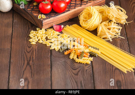 Satz von Zutaten für italienisches Abendessen. Sortiment von Raw-Typen und Formen von Nudeln in Tomaten cherry, Pilzen, Knoblauch, Gewürze Kräuter auf einer hölzernen zurück Stockfoto