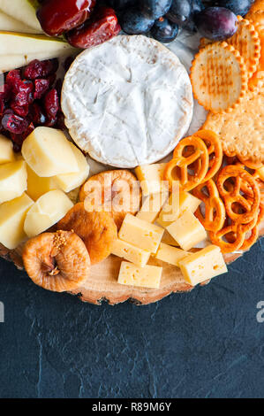 Käseplatte Traube trocken gesalzen Craker cookies Termine Cranberry, Feige, Birne Brezeln auf einem Holzbrett auf schwarzem Schiefer Hintergrund. Stockfoto