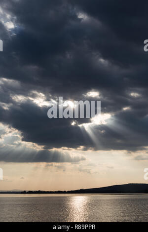 Schönen Sonnenuntergang an einem See, mit Sonnenstrahlen, die unter einem bewölkten Himmel Stockfoto