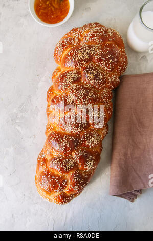 Hausgemachte Sesamsamen challah Brot, ein Glas Milch und Orange Marmelade auf einem weißen Hintergrund. Stockfoto