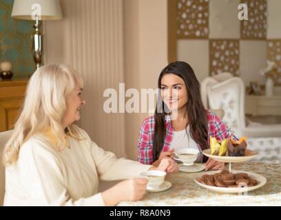 Junge Frau besucht Ihre ältere Mutter und Getränke Kaffee zusammen mit ihr. Zeit mit der Familie zusammen am Tisch, Tee trinken. Stockfoto