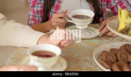Nahaufnahme von der Frau Hände halten eine Tasse Tee aus Keramik. Zarte weiße Porzellan Tassen und Teller Stockfoto