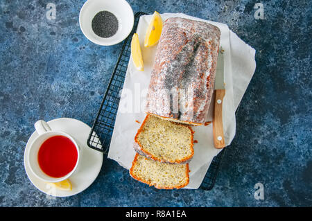 Hausgemachte lemon Poppy seed Pound Cake mit Glasur auf einem Gitter, eine Tasse roter Tee auf einem blauen Stein. Stockfoto