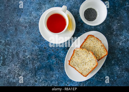 Scheiben von hausgemachten Zitrone Mohn Kuchen serviert auf einem weissen Teller, eine Tasse Tee auf einem blauen Stein. Stockfoto