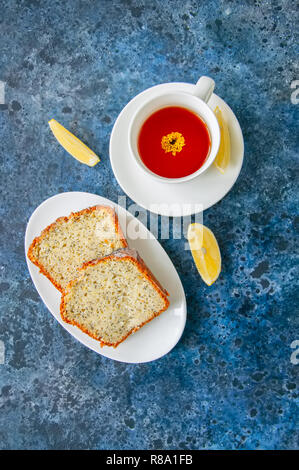 Scheiben von hausgemachten Zitrone Mohn Kuchen serviert auf einem weissen Teller, eine Tasse Tee auf einem blauen Stein. Stockfoto