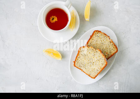 Scheiben von hausgemachten Zitrone Mohn Kuchen serviert auf einem weissen Teller, eine Tasse Tee auf einen weissen Stein Hintergrund. Stockfoto