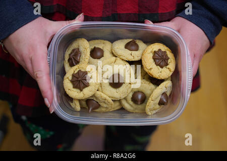 Weibliche home Baker hält ein Aufbewahrungsbehälter aus Kunststoff mit traditionellen Weihnachten Erdnussbutter gefüllten cookies Küsse Stockfoto