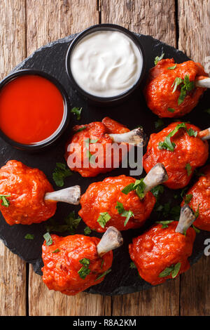 Warme Vorspeise Lutscher fried red Chicken Wings mit Saucen in der Nähe serviert auf einem Schiefer Board auf einen hölzernen Tisch. Vertikal oben Ansicht von oben Stockfoto