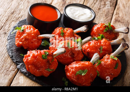 Warme Vorspeise Lutscher fried red Chicken Wings mit Saucen in der Nähe serviert auf einem Schiefer Board auf einem Holztisch. Horizontale Stockfoto