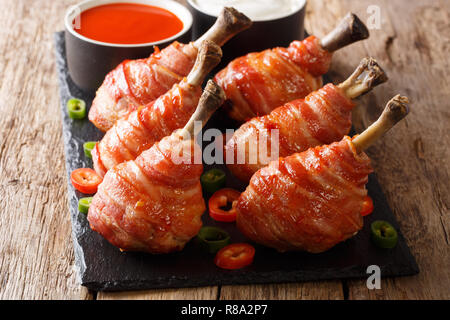 Rezept für Lutscher gegrillte Hähnchenkeulen in Speck mit Soßen schließen eingepackten auf einer Schiefertafel Board auf einem Holztisch. Horizontale Stockfoto