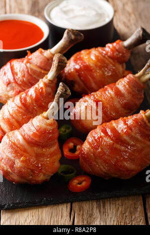 Köstliche Lutscher gegrillte Hähnchenkeulen in Speck mit Soßen serviert schließen eingepackten auf einer Schiefertafel Board auf dem Tisch. Vertikale Stockfoto