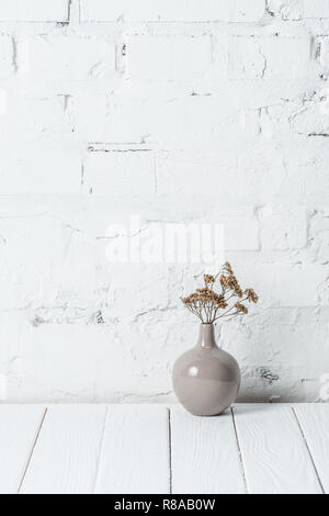 Bukett von getrockneten Blumen in Keramik Vase in der Nähe von White Brick Wall Stockfoto