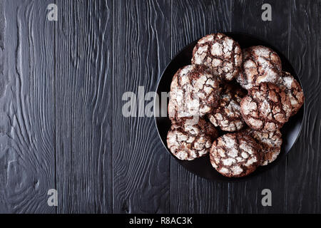 Schokolade Crinkle Cookies. Gebrochene Schokolade Kekse. Schokolade Kekse, Weihnachtsplätzchen auf einer schwarzen Platte auf einem Holztisch, Ansicht von oben, flach Stockfoto