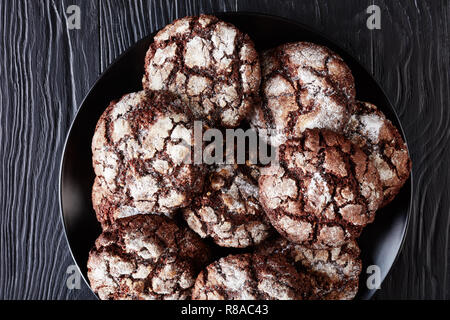 Close-up von Schokolade Crinkle Cookies. Gebrochene Schokolade Kekse. Schokolade Kekse, Weihnachtsplätzchen auf einer schwarzen Platte auf einem Holztisch, Ansicht von Stockfoto