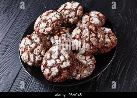 Close-up von Schokolade Crinkle Cookies. Gebrochene Schokolade Kekse. Schokolade Kekse, Weihnachtsplätzchen auf einer schwarzen Platte auf einem Holztisch, Ansicht von Stockfoto