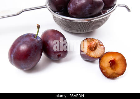 Stahl mit Fettaufsaugendem Süsse saftige Pflaumen, ganze und halbe reife Pflaumen mit Blatt vor dem Sieb auf einem weißen Hintergrund. Stockfoto