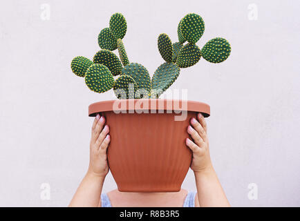 Die Frau ist mit großen roten Topf mit Opuntia Kakteen auf Kopfhöhe. Konzeptuelle Realismus gesichtslosen Portrait Stockfoto