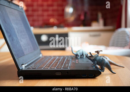 Laptop auf Holztisch mit kleinen Dinosaurier Spielzeug, die scheinen auf den Bildschirm schauen. Natürliches Licht. Von der Seite. Stockfoto