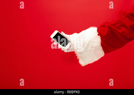 Santa Claus holding Mobiltelefon bereit für Weihnachten auf Roten studio Hintergrund. Die Jahreszeit, Winter, Urlaub, Feier, Geschenk Konzept Stockfoto