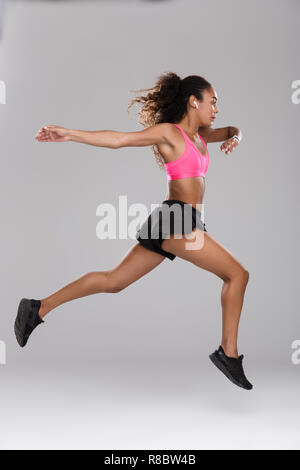 In voller Länge Porträt einer starken jungen afrikanischen Sportlerin Übungen über grauen Hintergrund isoliert, Aufwärmen, springen Stockfoto