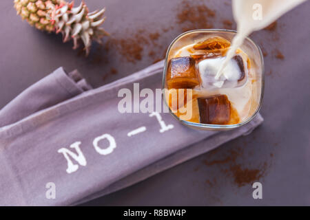Gießen Milch in ein Glas Eiskaffee Würfel auf dunklem Hintergrund. Buchstaben Nummer 1 und Pinapple Stockfoto