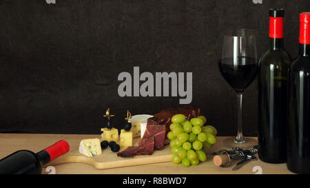 Köstliche Komposition eine Flasche und ein Glas Rotwein mit Käse, Schinken und Trauben Stockfoto