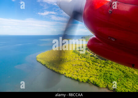 Flugreisen in Fidschi, Melanesien, Ozeanien. Blick auf einen grünen tropischen Insel aus einem Fenster eines kleinen Turboprop Propeller rot Motor Flugzeug fliegen Stockfoto