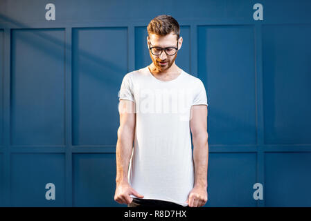 Porträt eines gutaussehenden Mann im weißen T-Shirt mit Leerzeichen einfügen, die auf der blauen Wand Hintergrund zu kopieren Stockfoto