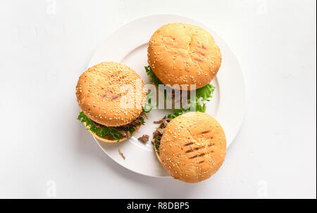 Hamburger zog Rindfleisch mit Gemüse auf die Platte über der weißen Stein Hintergrund. Ansicht von oben, flach Stockfoto