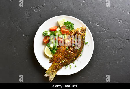 Gekochter Fisch vom Grill mit gesunden Salat von frischem Gemüse auf die Platte über der schwarzen Stein Hintergrund mit kopieren. Ansicht von oben, flach Stockfoto